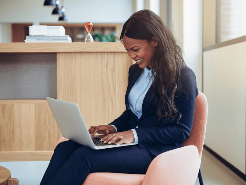 Young African-American businesswoman laughing while working online with a laptop in the lounge of an office.
