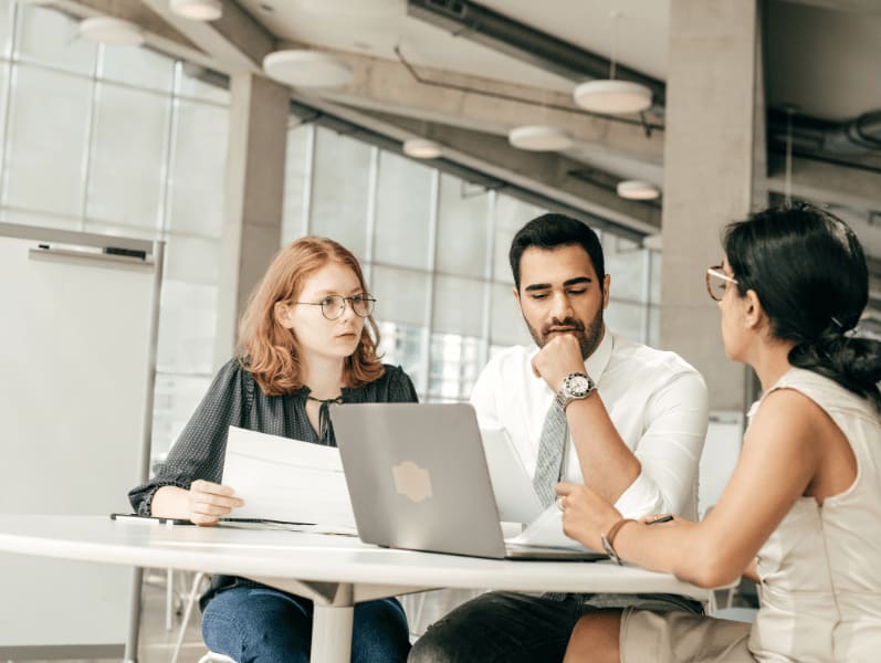 The team member sitting around table in front of lap top discussing