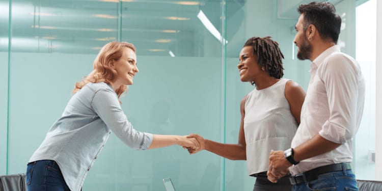 Entrepreneur greeting her business partner with firm handshake while having negotiations in modern boardroom.
